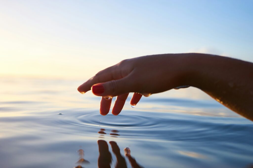 A hand skims over the surface of water, creating a ripple.