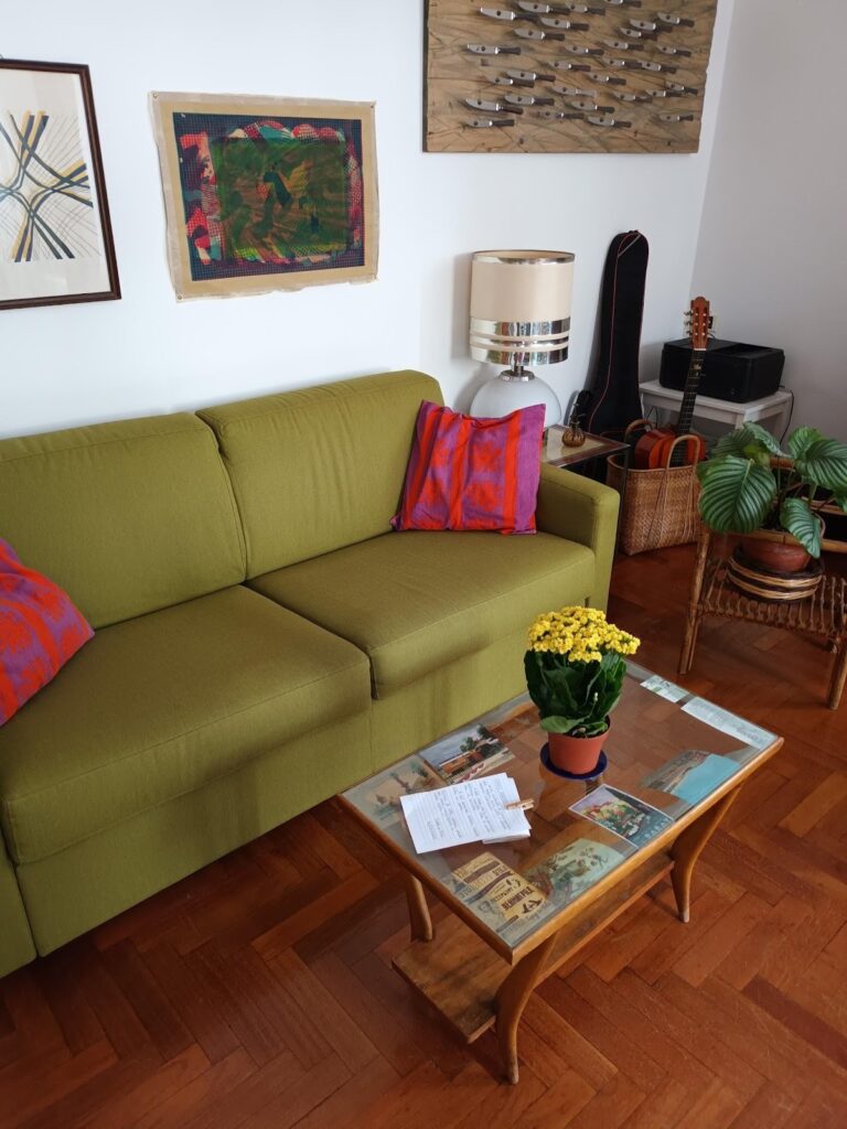 A living room, simply decorated, the focal  point being a green couch and colorful pillows. 