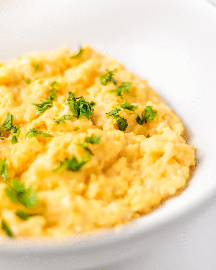 A close-up shot of a bowl of scrambled eggs adorned with fresh herbs. 