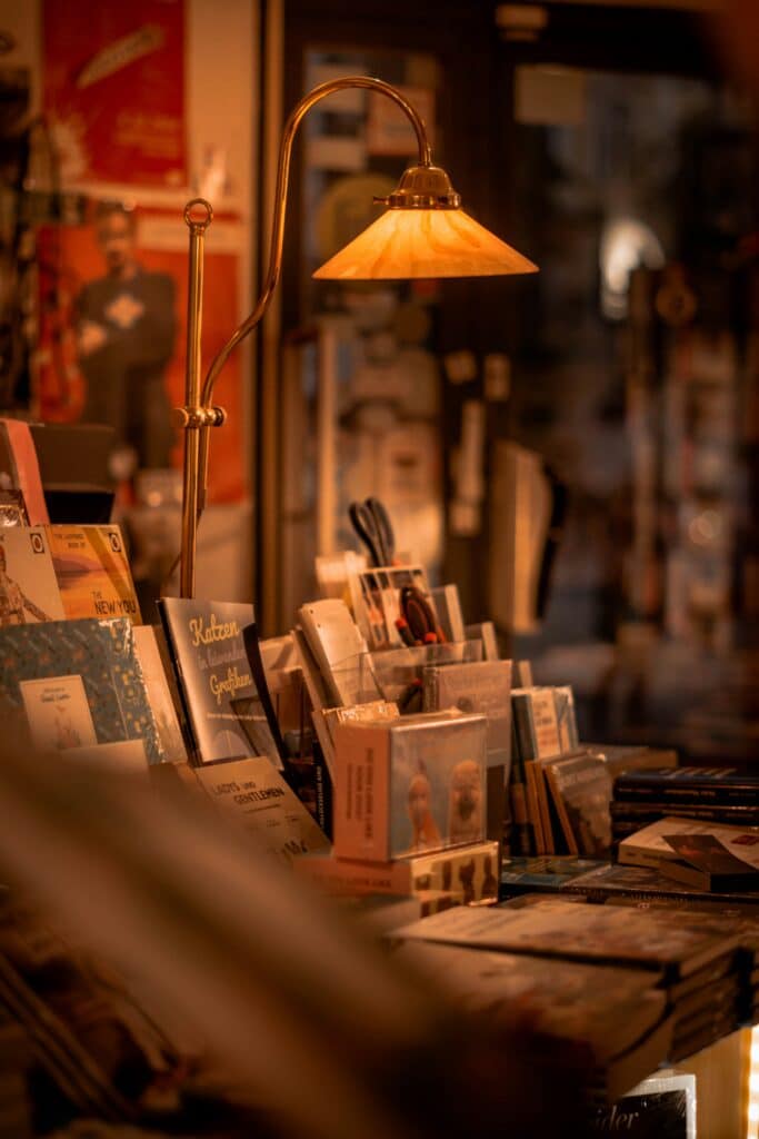 A brass table lamp with a warm glow over books and other odds and ends at a small shop.