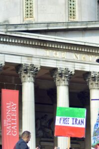An Iranian flag held aloft and bearing the slogan ‘Free Iran’ in front of Britain’s National Gallery, with a man standing in the foreground.