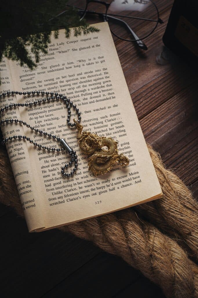 A golden dragon pendant with a silver chain lying on a book.