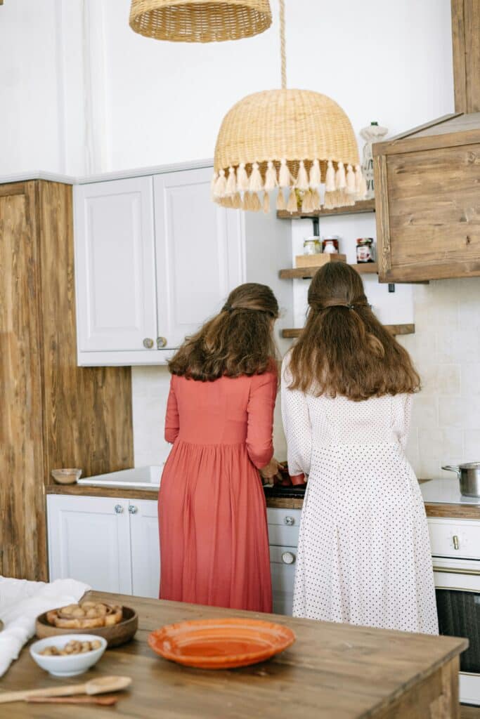 Two women standing with their backs turned in the kitchen, cooking over the stove top.