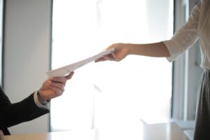 A woman hands her application documents to the interviewer.