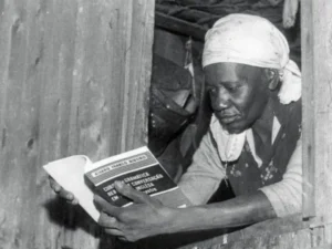 Brazilian Writer Carolina Maria de Jesus reading a book out of a small window.