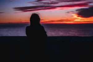 A shadowed woman gazes at a sunset across the seemingly endless ocean.