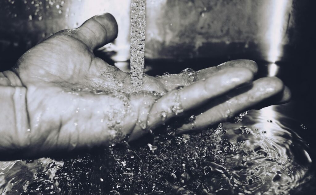 A grayscale image of a man washing his hand. It is large, strong, and he lets the water cleanse it thoroughly.