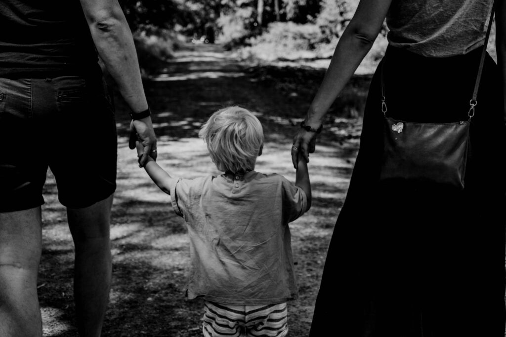 Parents walk down a trail with their child between them as each one holds their child’s hands.