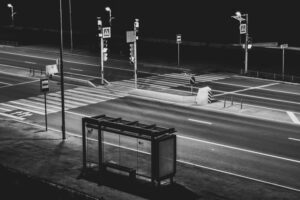 A black and white photograph of a bus stop and intersection at night.