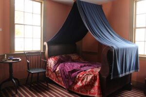 Blue canopy over red-blanketed wooden bed.
