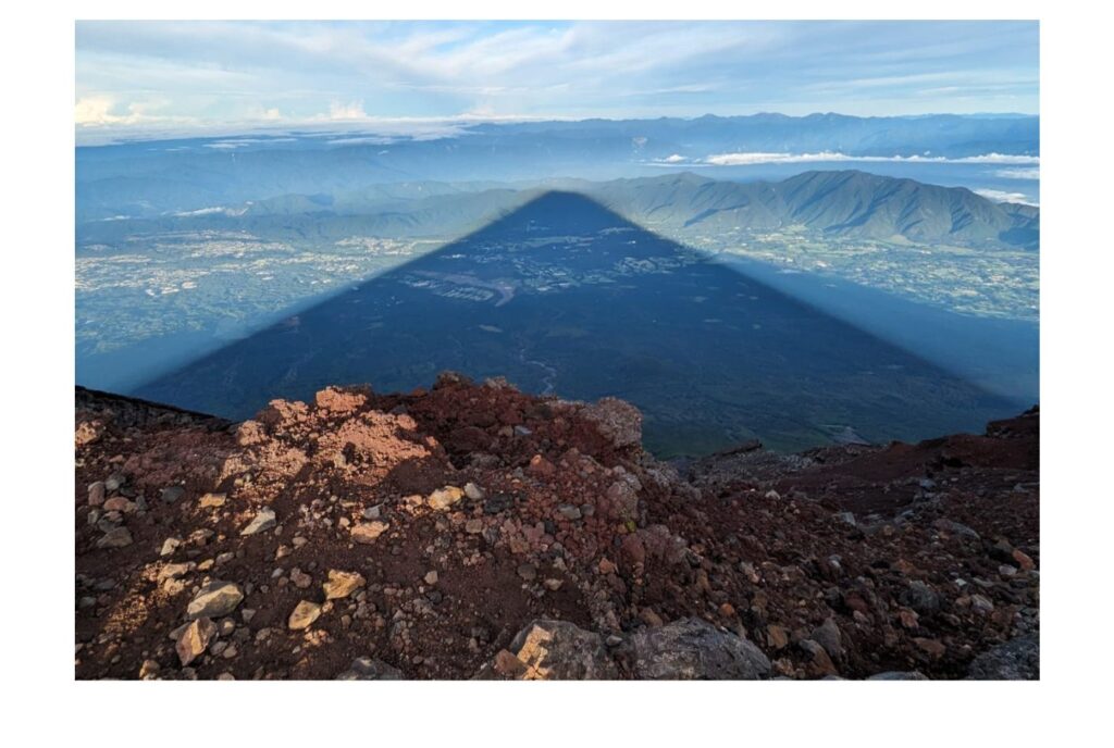 Image shows a combination of two photos: the first is a landscape shot of Mount Fuji during summer, the second shows the shadow of Fuji spread over the land.