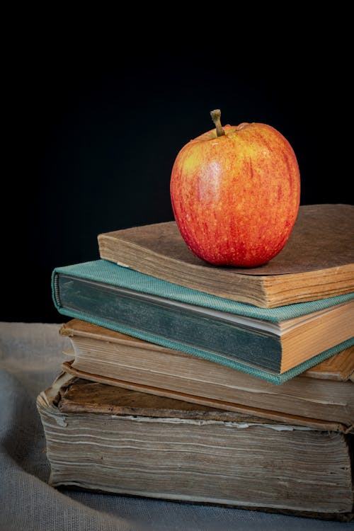 A stack of older-looking books with an apple perched on top.