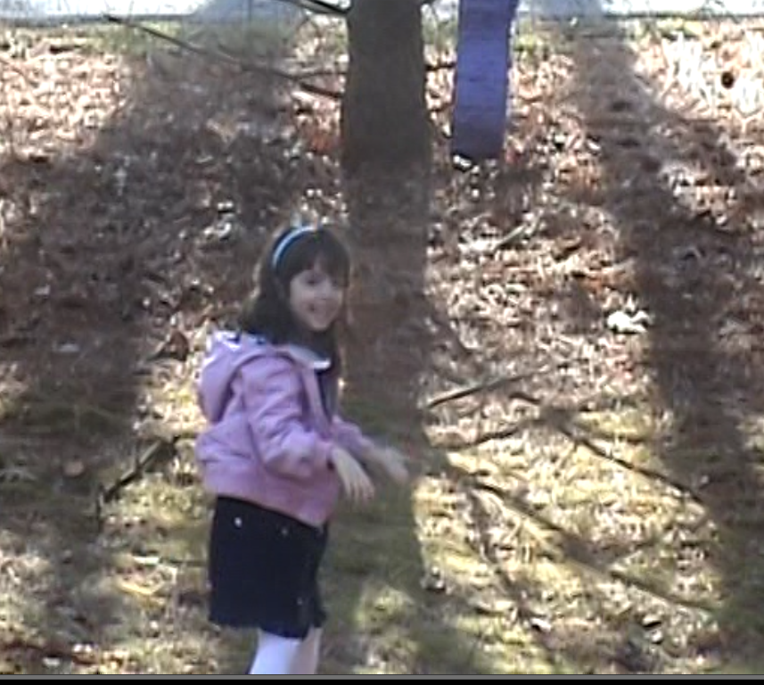 A 6-year-old girl smiles at the camera; she is ecstatic to take a turn at hitting a piñata at her birthday party. 