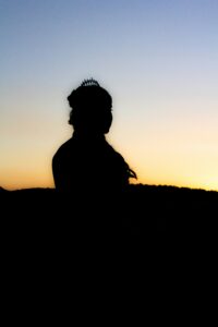 Silhouette of a woman wearing a tiara and gazing at the sunset.