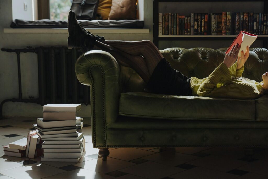 A woman lying on the couch reading, surrounded by books.