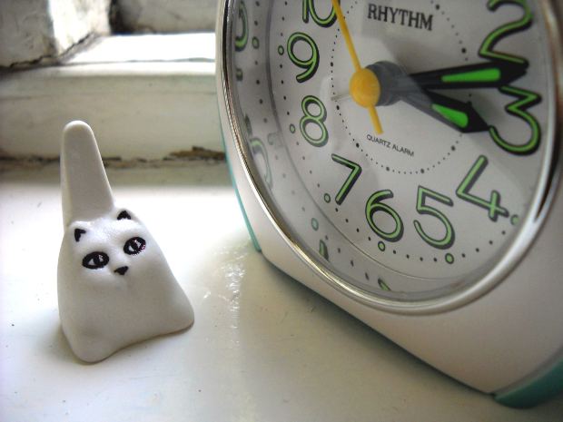 Ceramic cat guards an alarm clock.