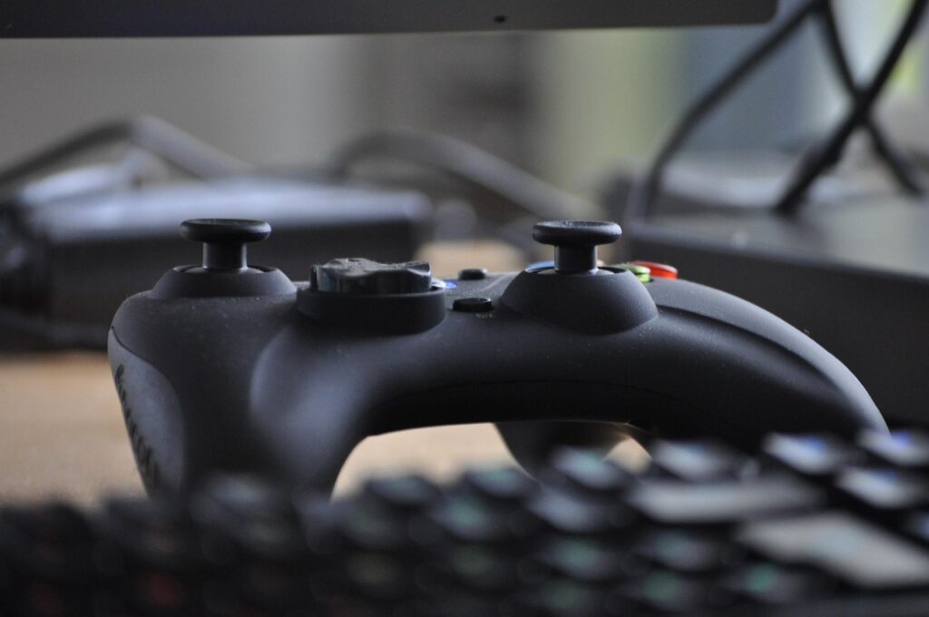 An X-Box gaming controller sitting on a desk in front of a keyboard.