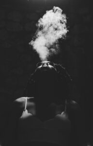 A woman, dressed in her nightgown, face turned towards Heaven, breathes out smoke.