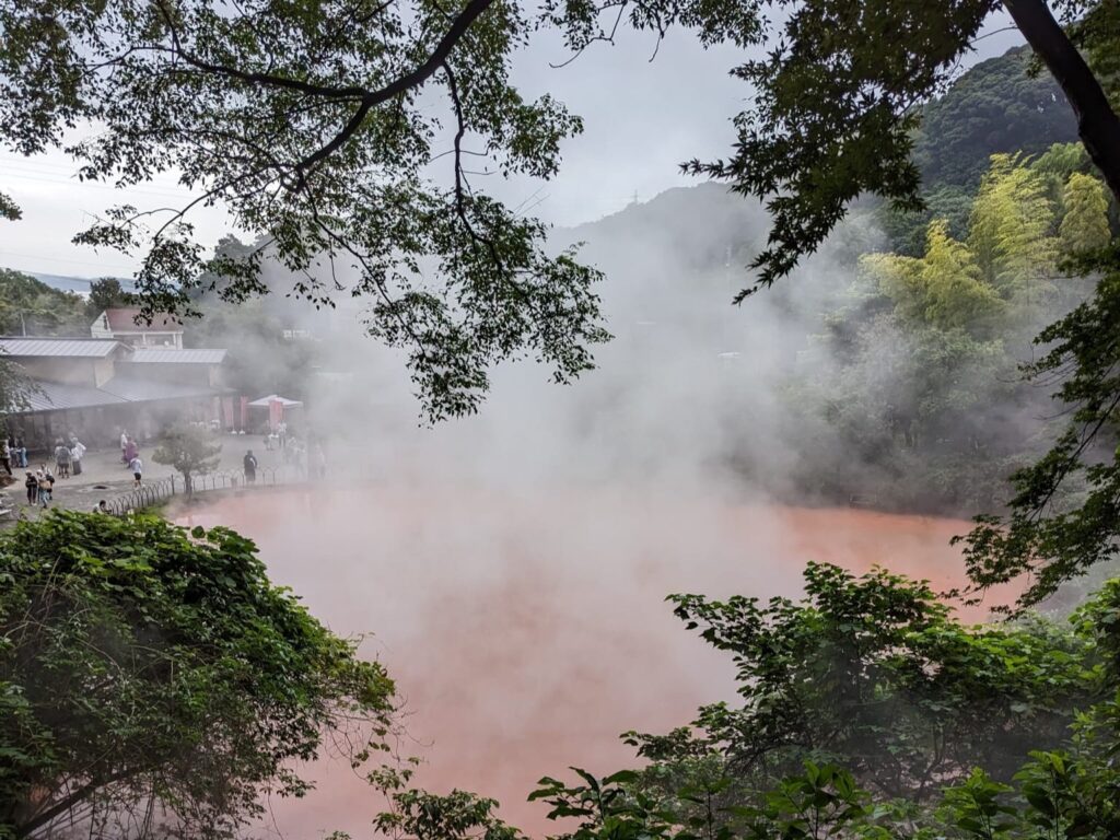 An image of steam rising from a hot spring with red water.