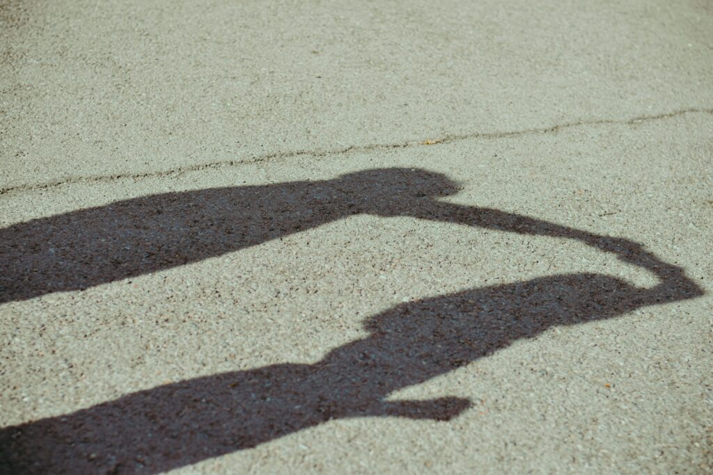 Two shadows, cast long on the pavement are connected as the first pulls the second forcefully by her arm. They are arguing.