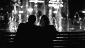 Image of a couple sitting on a bench, looking at a fountain, in black and white.