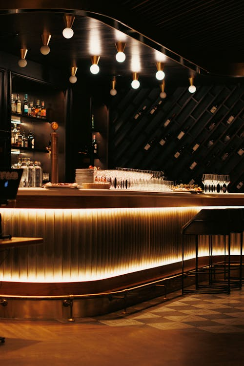 A low-lit, darkly colored bar full of wood and wine glasses. There are lights hanging above like little stars.