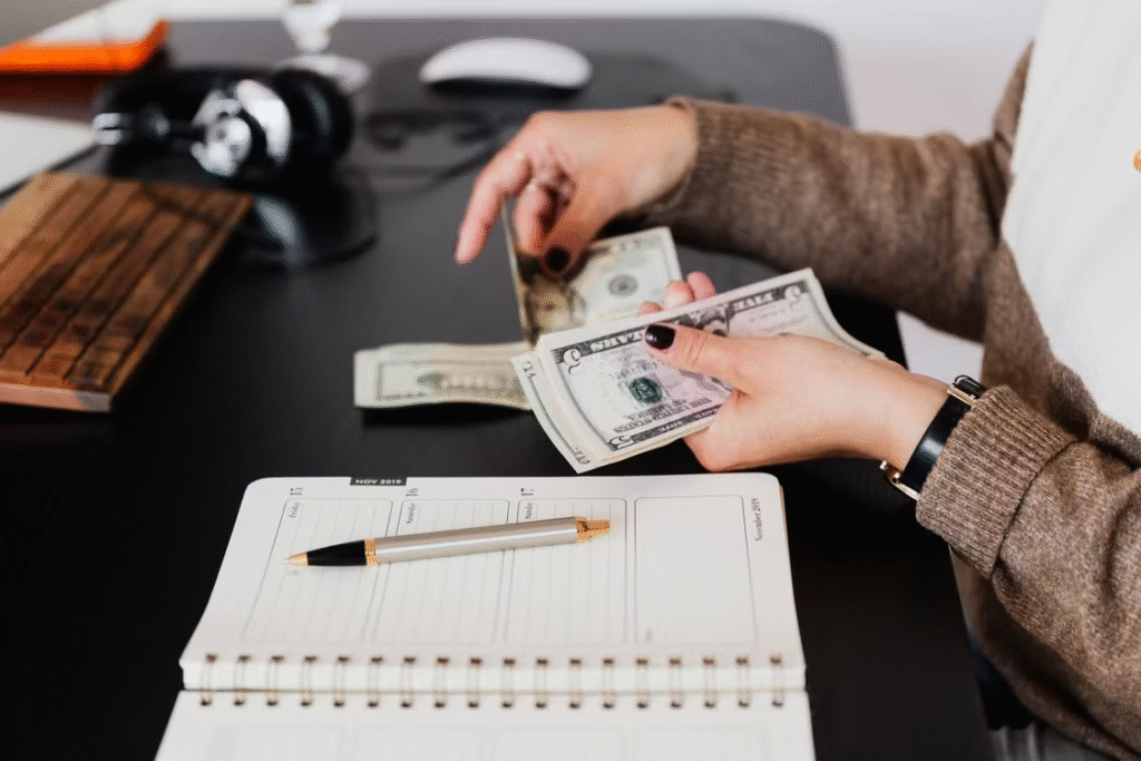 Woman counting money with a notebook, pen, and headphones nearby.