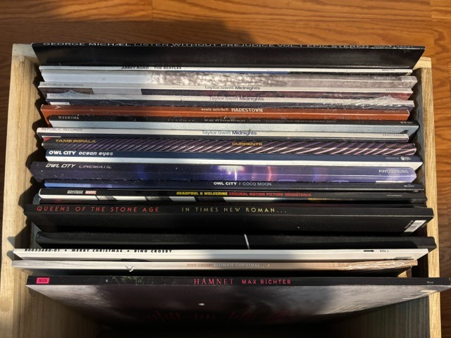 A wooden crate filled with a unique collection of records of different artists.